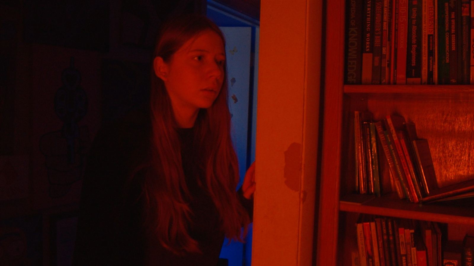 Emily peers around a doorway beside a bookshelf lit in red and blue.